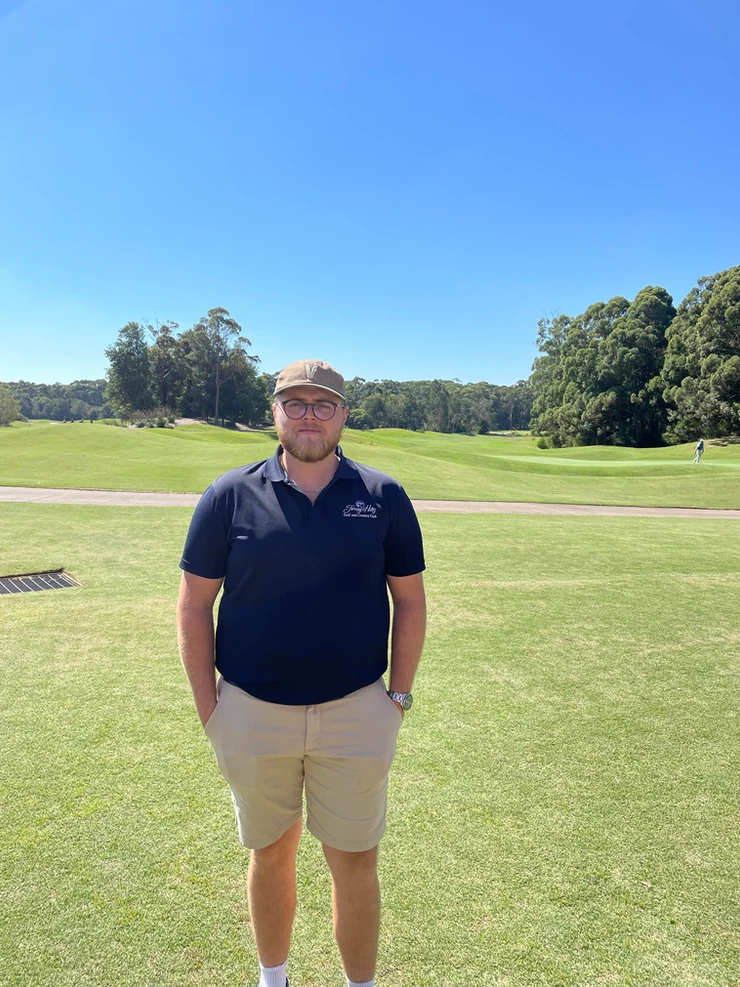 a man is standing on a golf course with his hands in his pockets .