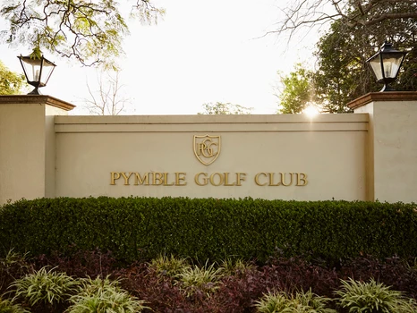 A sign for the pymeble golf club is surrounded by bushes and trees